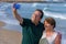 Modern sweet and loving hispanic mature couple taking selfie portrait- senior retired husband and wife on their 70s enjoying beach