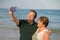 Modern sweet and loving hispanic mature couple taking selfie portrait- senior retired husband and wife on their 70s enjoying beach