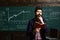 Modern teacher hipster writing on big blackboard with math formula. University students studying with books in library