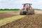 Modern tech red tractor plowing a green agricultural field in spring on the farm. Harvester sowing wheat.