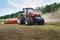 Modern tech red tractor plowing a green agricultural field in spring on the farm. Harvester sowing wheat.