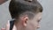 A modern teenage hairstyle in a barber shop. A close-up of the hands of a hairdresser who shaves a strip over the ear of