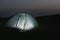 Modern tent lit from inside in wilderness at night. Overnight camping