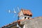 Modern three way TV antenna mounted on partially rusted metal pipe next to white brick chimney on top of family house