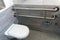 A modern toilet room with a toilet bowl and a toilet paper holder. Metal vandal-proof toilet accessories and handrails for the