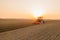 Modern tractor cultivates soil in field at bright sunset