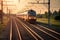 A modern train traveling on a track with golden sunlight. The train is orange and silver