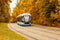 Modern tram on the background of autumn foliage. Rail ecological city transport on the background of the autumn landscape,