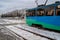 Modern tram riding in winter city. Contemporary blue and green tram riding on snowy rails on cloudy winter day in city