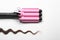 Modern triple curling iron and brown hair lock on white background, top view