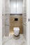 Modern wall-mounted white toilet bowl, black button the background of a beige bathroom wall. Part of the interior of the