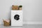 Modern washing machine with houseplant and laundry baskets near white wall. Space for text