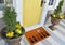 Modern Welcome zute doormat with small black plants and watering colorful plant outside home with yellow flowers and leaves