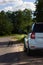 A modern white car sits at the edge of the road next to a green field while traveling and looking for new routes. Outdoor weekends