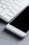 Modern white mobile phone and computer keyboard on a gray aluminum background