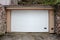 Modern white rollup garage doors with small handle for manual opening mounted on renovated garage wall surrounded with traditional