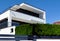 Modern white stucco cube shaped residential building with long balcony and evergreen hedge