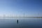 Modern windmills in the water near the shore along a green grassy dike