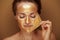 Modern woman removing golden mask against beige background