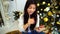Modern Women Using Smartphone And Plastic Card Orders Online Gift and Sits on Background Decorated Christmas Tree and