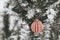 Modern wooden bauble hanging on snowy pine tree branch. Decorated christmas tree with stylish ornaments in snow outdoors. Winter