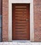 Modern wooden door in red brick wall with narrow horizontal window panes and downspout