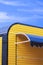 Modern yellow and black corrugated steel coffee street kiosk with blue awning against cloud on blue sky background