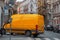 Modern Yellow Delivery Truck Van In European Town At Cityscape Background
