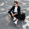 Modern young hipster man in dark sunglasses in fashionable clothes in a white shoes relaxes sitting on the rubber wheel