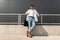 Modern young man hipster in fashionable summer white clothes in sunglasses in stylish red leather sandals with a bag stands