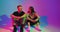 Modern young teen couple sitting and talking in colourful neon studio light. Romantic dating and flirting. Copy space