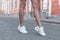 Modern young woman with slender beautiful legs in fashionable white sneakers walks down the street. Stylish sporty women`s shoes.