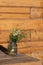 Modest bouquet of white and pink wildflowers with green twigs in glass jar is placed on wooden table in oudoor.