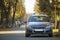 Modified image of a fictional non existent car. Car parked in quiet area on asphalt road on blurred green and yellow trees bokeh