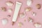 Moisturizer cream squeeze cosmetic tube with long nozzle and a lot of different sea shells on pink background. Natural organic