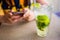 Mojito with ice, mint and lime in glass close up. Lady using mobile in cafe