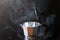 Moka pot brewing hot coffee and smoke on black background