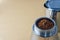 Mokapot coffee brewing with ground coffee beans isolated on brown background
