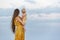 Mom in bright dress and with long hair holds baby and looks at the sea. Maternity concept