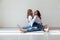 Mom brunette and daughter blonde in jeans sit on the floor