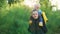 Mom carries her child in the park at sunset, in a yellow jacket, they are laughing happily.