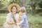 Mom with a child walks in a couple. She holds flowers and baguette and the child also holds baguette