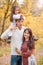 Mom, dad and daughter walk through the autumn forest. Daughter sits on father`s shoulders