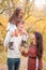 Mom, dad and daughter walk through the autumn forest. Daughter sits on father`s shoulders