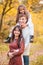 Mom, dad and daughter walk through the autumn forest. Daughter sits on father`s shoulders