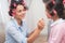 Mom and daughter in beauty salon. They have curlers in their hair. Mother dye lips to her doughter.