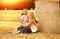 Mom and daughter Caucasians sitting together on a mown wheat field where there is a huge sheaf of hay enjoying nature at sunset.