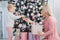 Mom and daughter decorate the Christmas pink tree indoors.