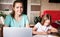 Mom and daughter do school lessons together. Mom looks at the camera and smiles