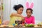Mom and daughter with funny bunny ears filming on phone them painting eggs. African American woman and little girl are